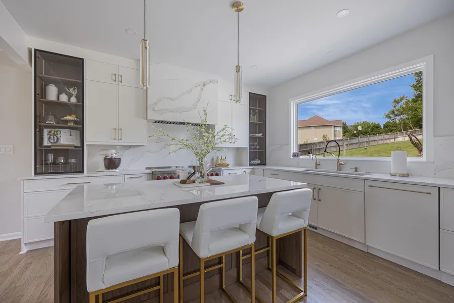 Finished white kitchen with a marble island, gold accents and bar seating